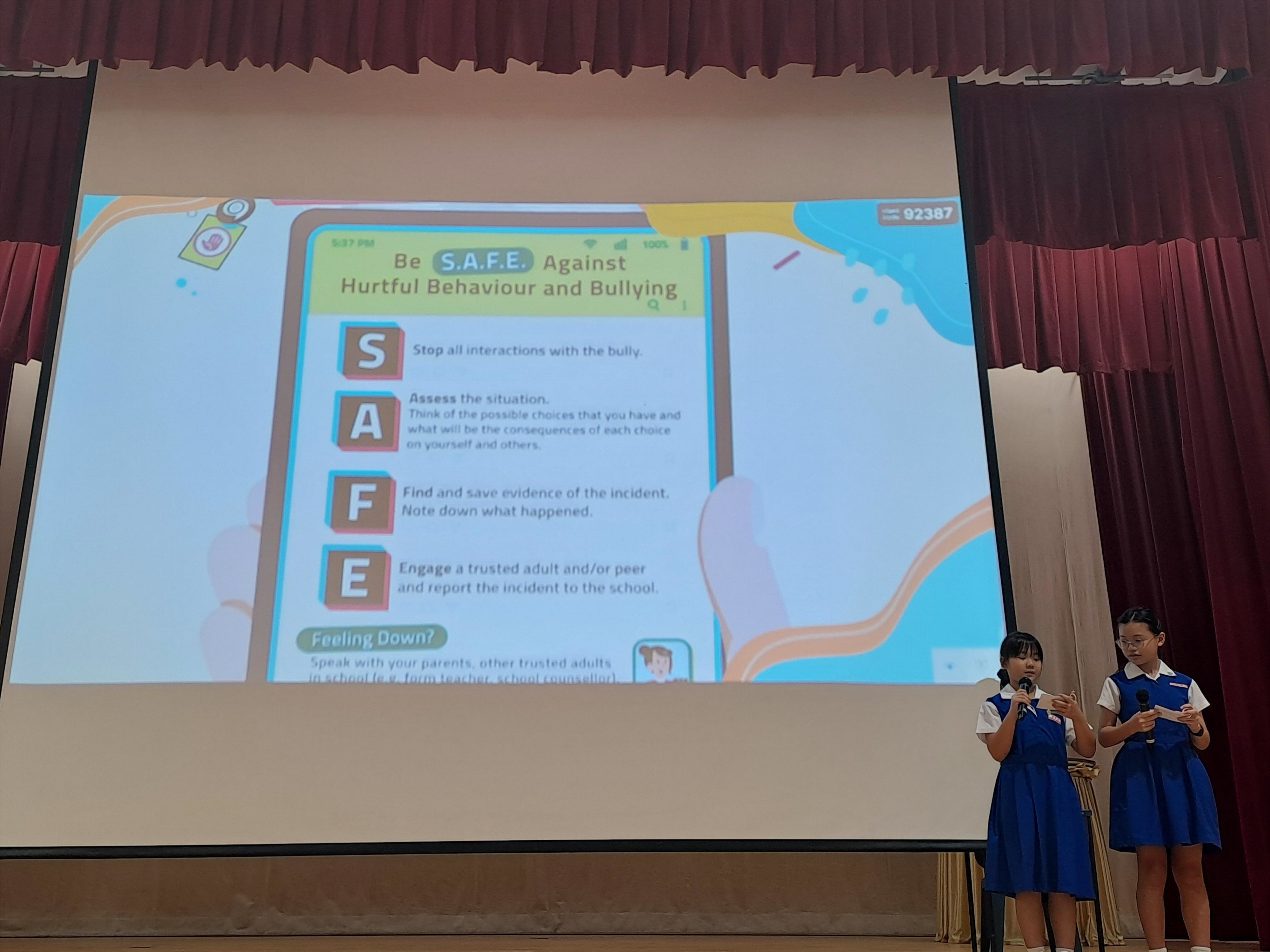 Pupil leaders in school uniform facilitating on stage on ‘Be S.A.F.E against hurtful behaviour and bullying' 